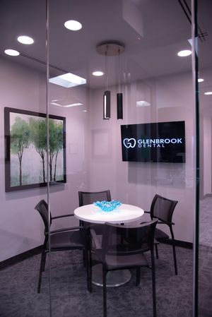 A glass-enclosed meeting room at Glenbrook Dental with a meeting table and a screen on the wall