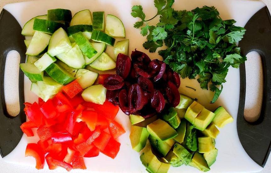 Cutting board with olives, cilantro, red pepper, cucumber, and avocado