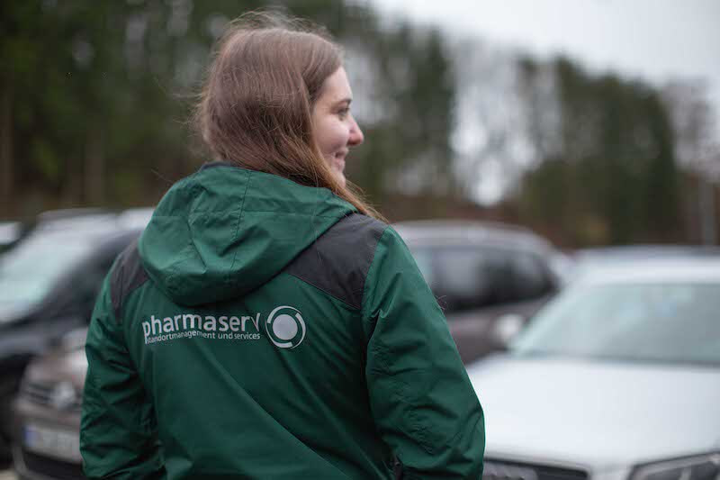 Caucasian female standing with her back faced to the viewer wearing a green pharmaserv jacket.