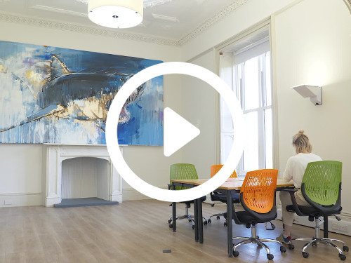 Spacious meeting room with wall mounted art painting of shark opposite wooden table with green and orange mesh chairs Skype background