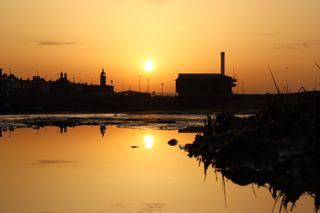 Sunrise between Shoreham lighthouse and Shoreham life boat station being reflected in a rock pool.