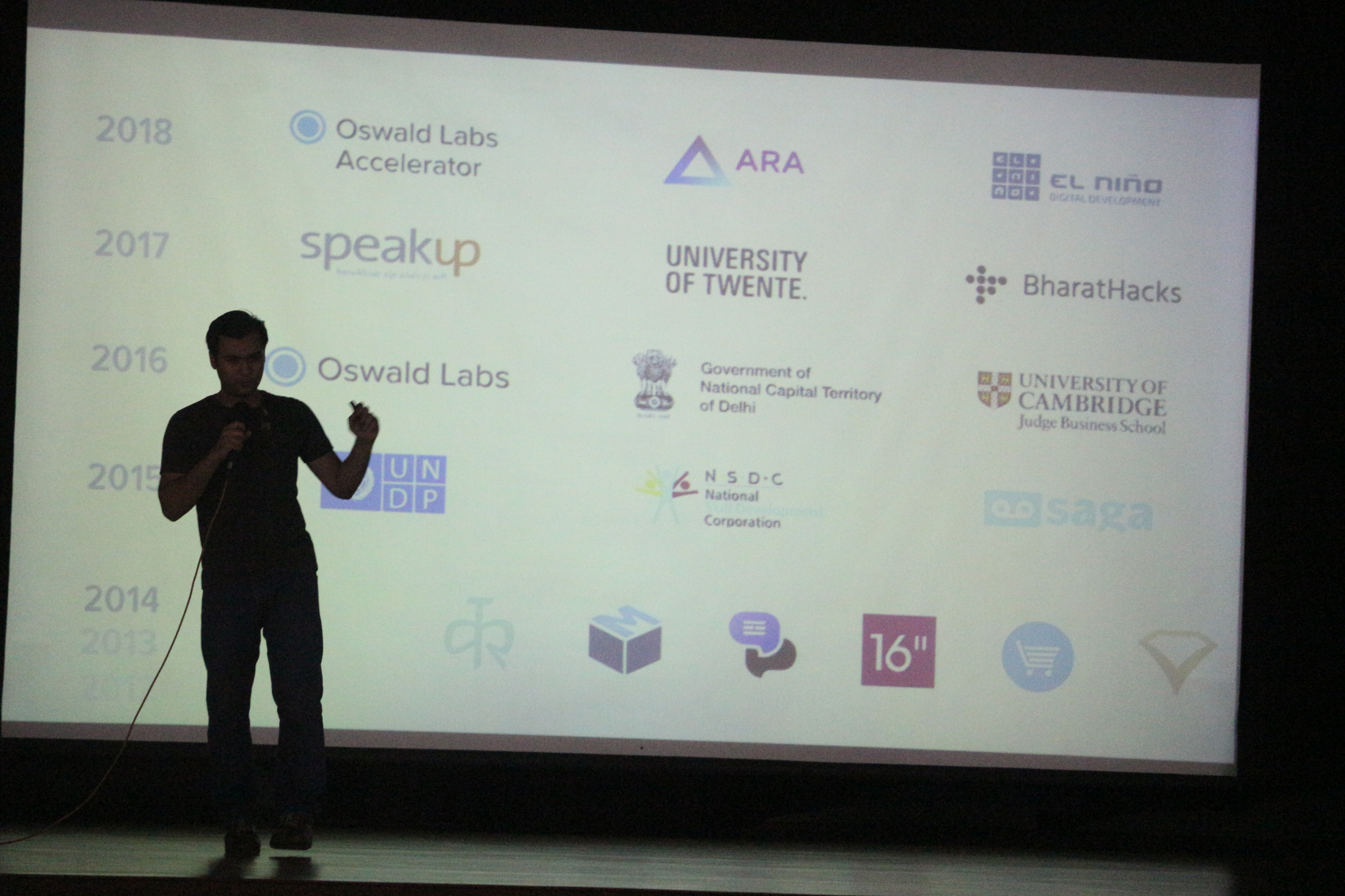 Anand Chowdhary speaking behind a set of logos
