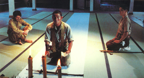 A screenshot of three men on their knees praying to an alter in a Japanese ceremonial hall shown from the front. From the film 'Merry Christmas, Mr. Lawrence'.