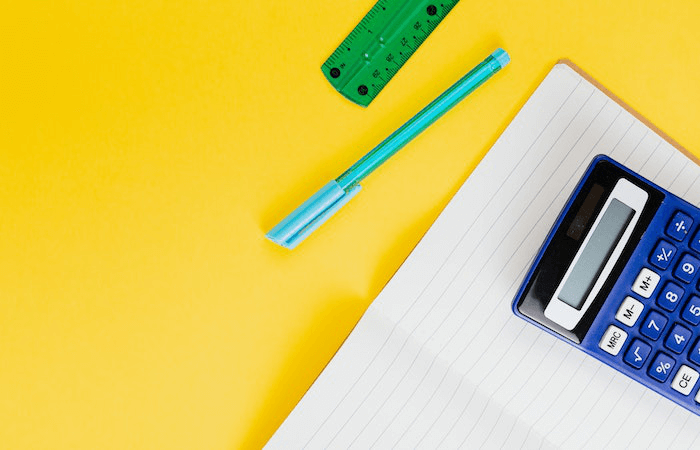 yellow desk with a calculator, pen, paper and ruler