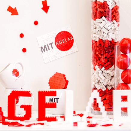 Various objects - a coffee mug, a jigsaw puzzle, legos, and stressballs - all branded with MIT AgeLab branding.
