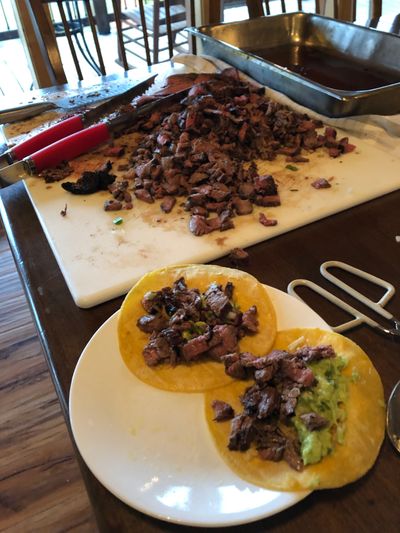Two steak tacos alongside a cutting board of chopped carne asada