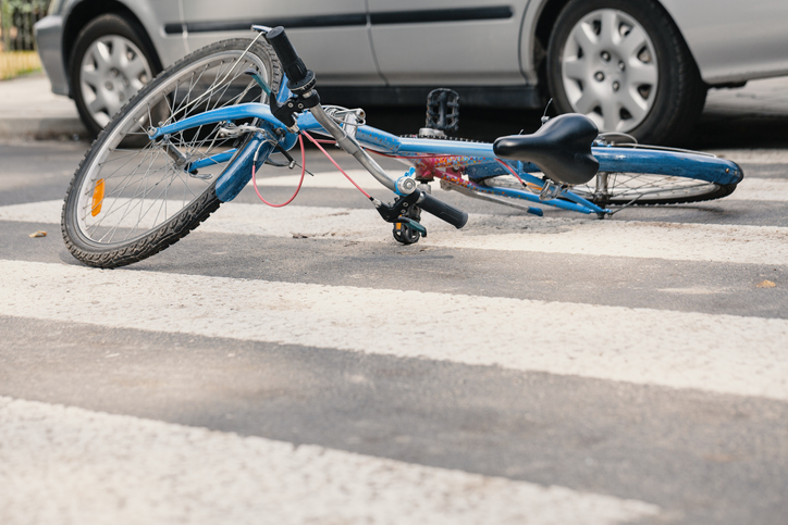 a blue mountain bike lying in a crosswalk with pieces of debris