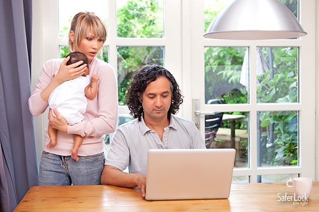 A couple with a newborn baby look at a laptop screen together with concern.