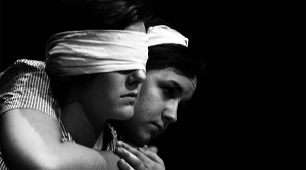a woman with bandage over her eyes,
and another hugging her from behind