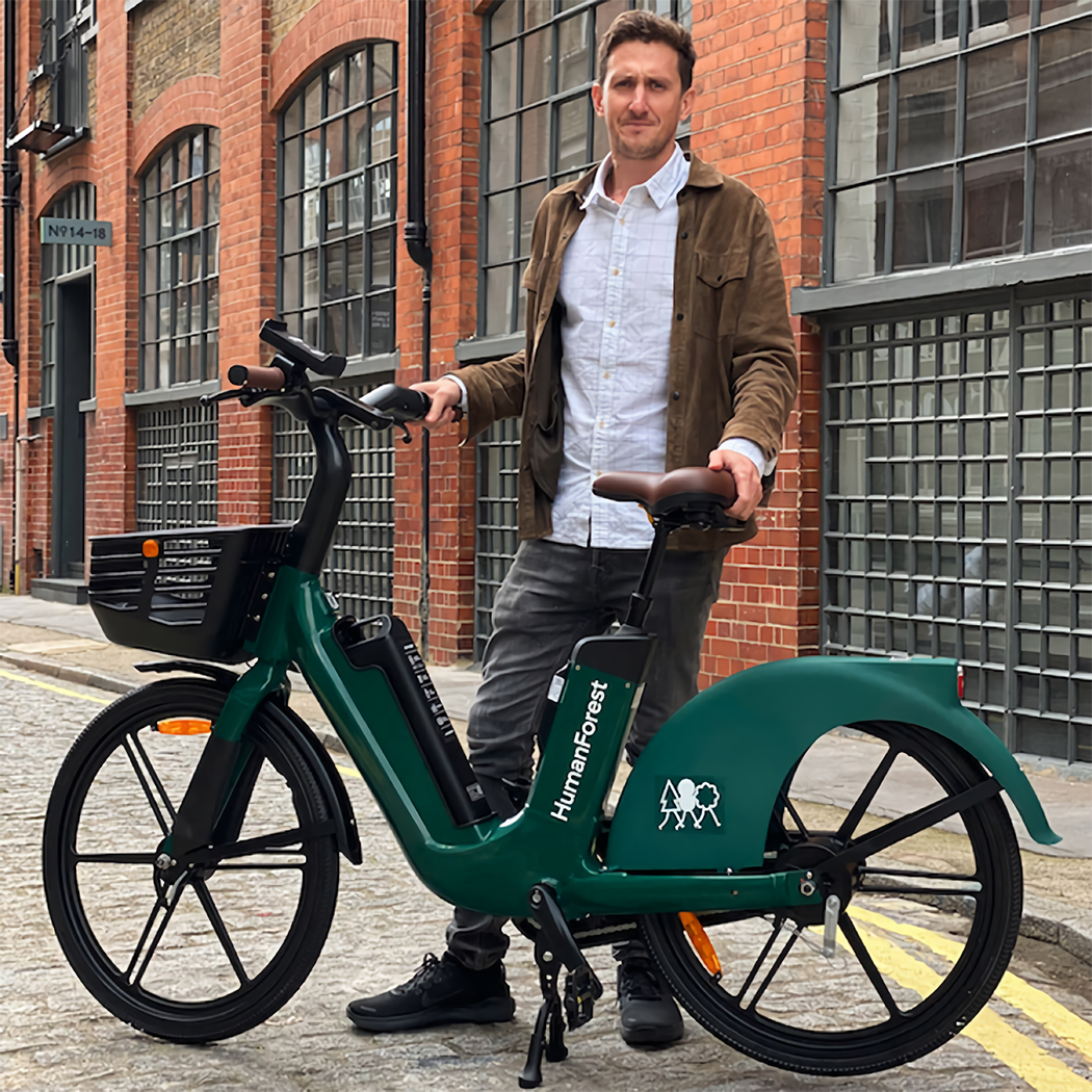 Agustin Guilisasti, Founder & CEO of Human Forest standing on a street in the middle of London holding a green human forest OKAI e-bike.