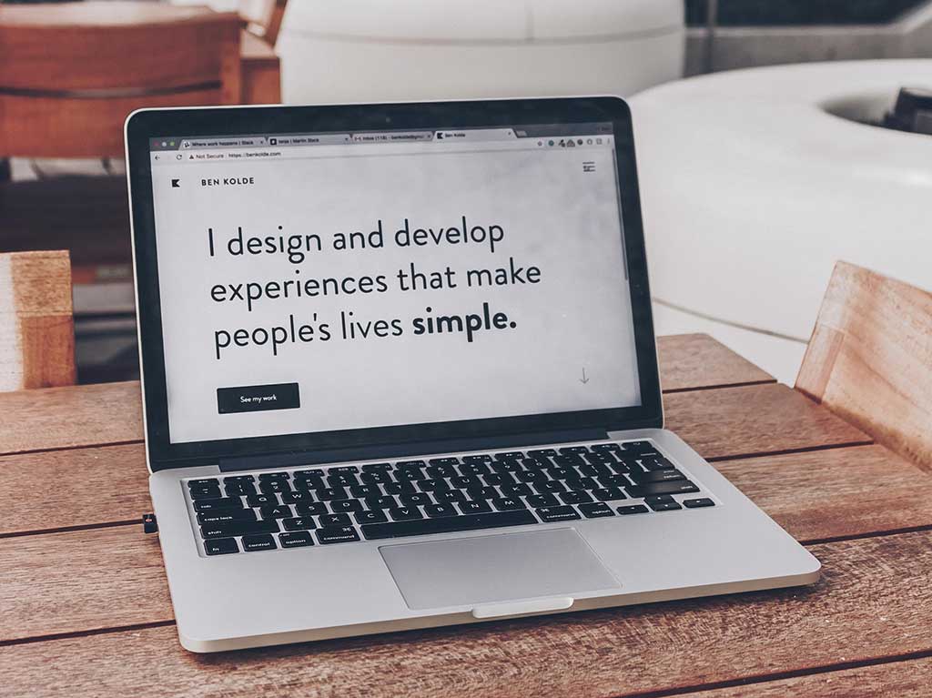 A laptop on a table with the message I design and develop experiences that make peoples lives simple on the screen. Photo by Ben Kolde on Unsplash.