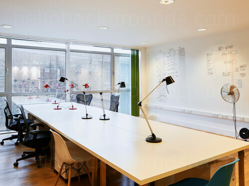 Simple shared workspace featuring whiteboard by long wooden table with adjustable reading lamps and office chairs Skype background