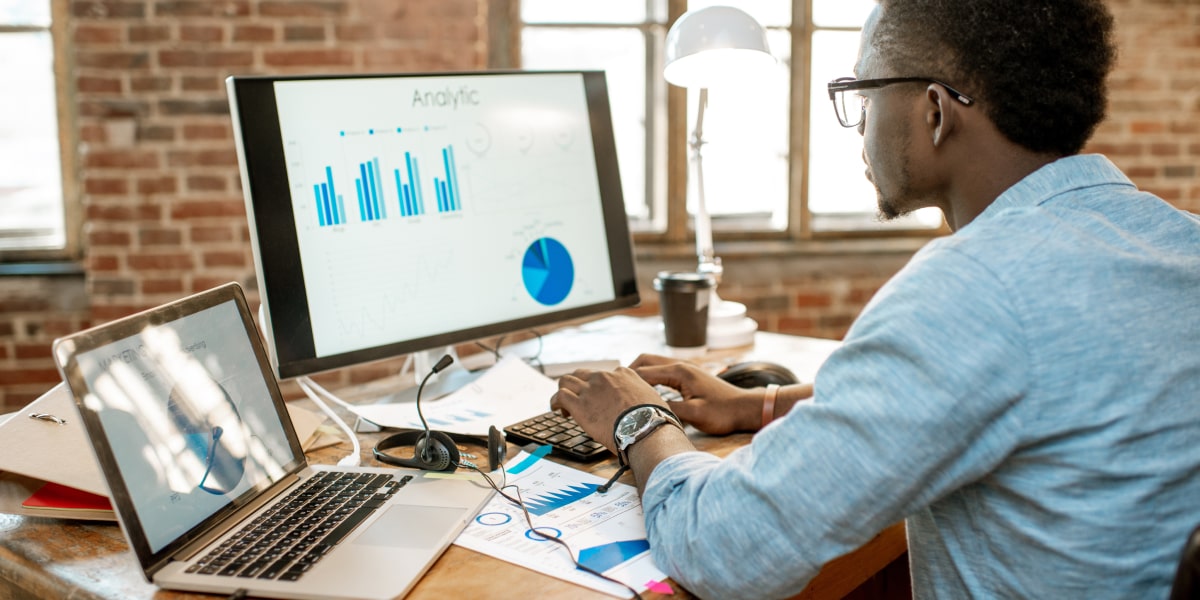 What's the difference between descriptive and inferential statistics? A data analyst sitting at a desk looking at a graph on a desktop computer