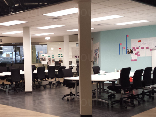 Spacious pillared shared workspace featuring large white tables with black office chairs Zoom background
