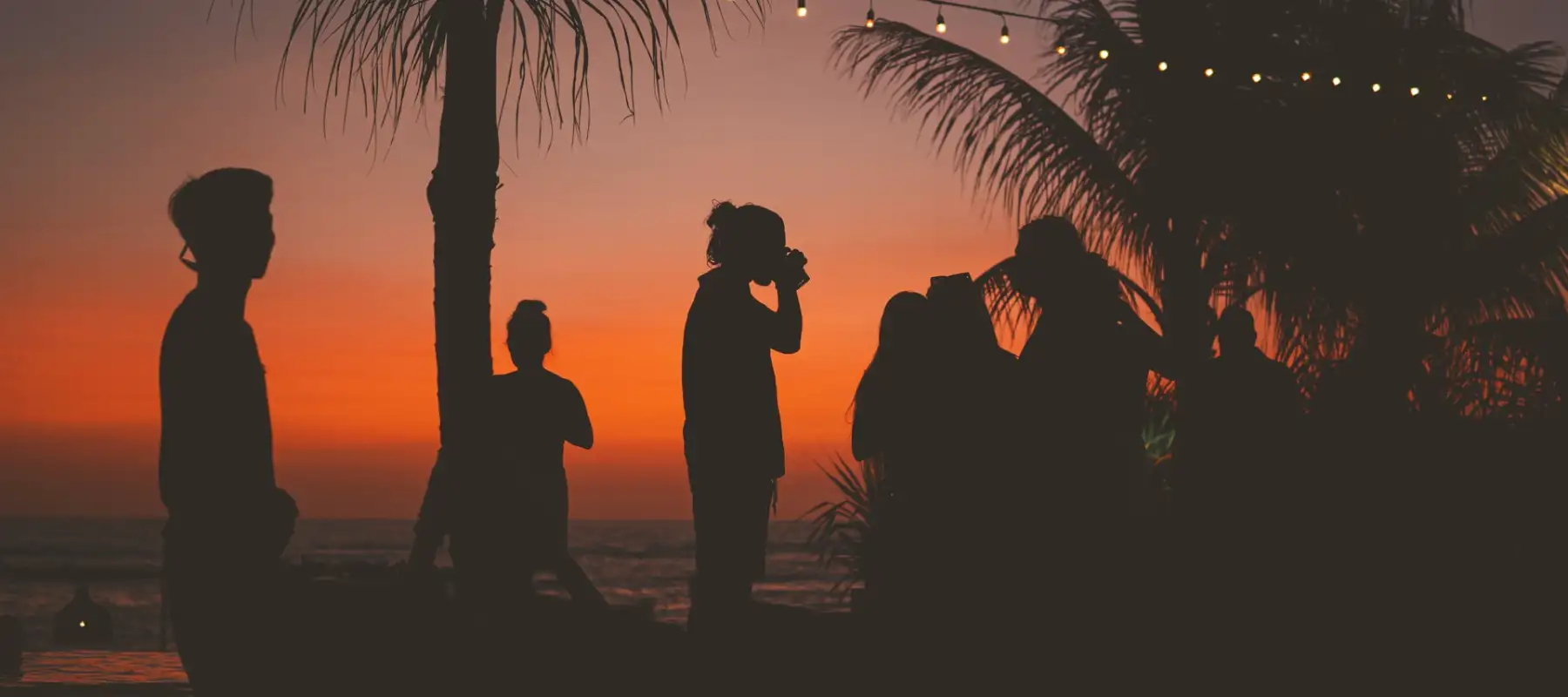 Foto de um por do sol com silhueta de pessoas em uma festa ao ar livre