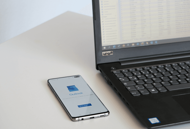 Smartphone mit Outlook-App neben einem Laptop