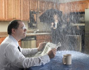 man sitting in his kitchen, reading a newspaper, as water comes down from the ceiling
