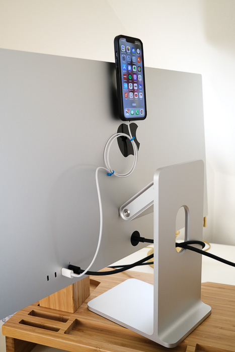 An Apple Studio Display with a MagSafe charger attached to the back using 3M Command Strips and an iPhone 13 mounted to the MagSafe charger