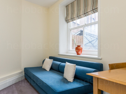 Small and simple cream walled living room featuring blue sofa and wooden desk with chair Zoom background