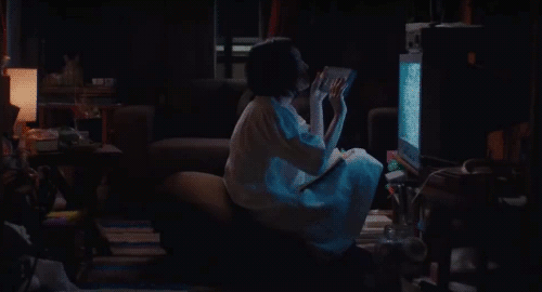 An animated gif of a scene from the movie 'Kumiko The Treasure Hunter' of Kumiko inserting a VHS tape into the VHS player while sitting close to her TV.