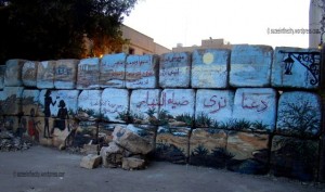 [Alaa Awad’s mural captured at sunset. Behind the wall, barbwires and idle military policemen fill the empty space]