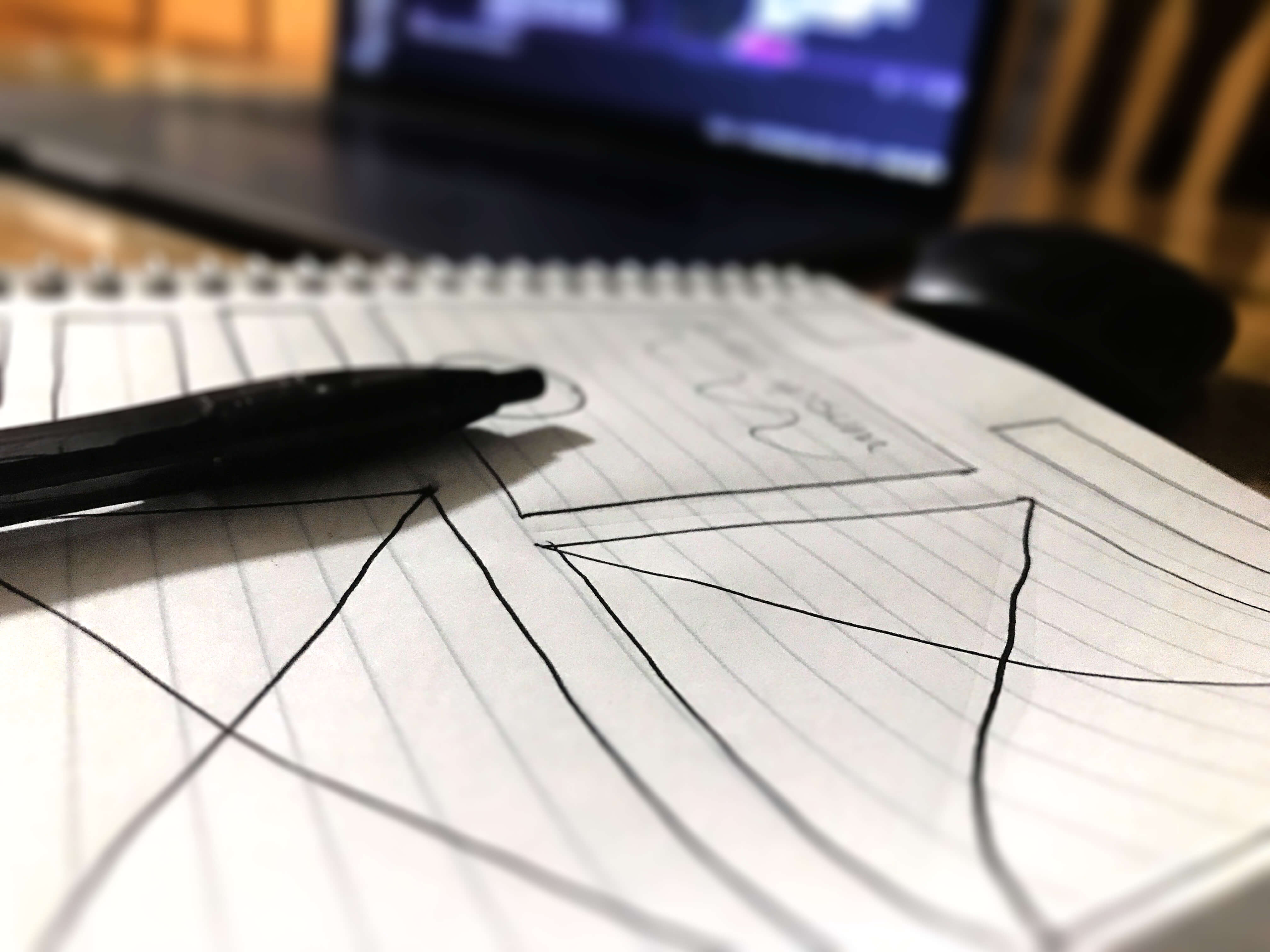 A pen laying on top of paper with a wireframe drawn on it.