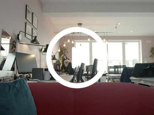 Spacious well lit office containing modern red sofa in front of multiple white computer desks with and black office chairs Google Meet background