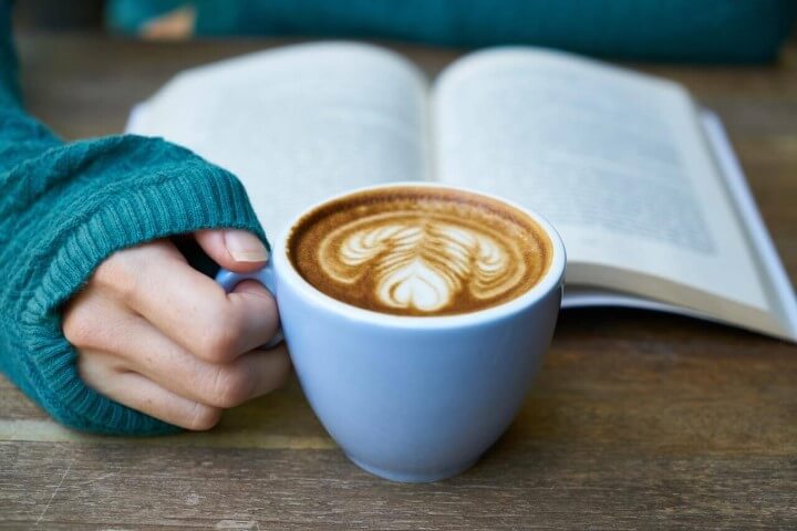 Image - hand holding coffee cup on desk with open book