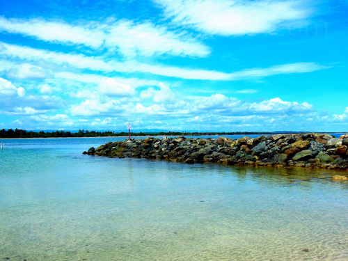 Shallow water with prominent rocky breakwater and bright blue sky with clouds Zoom background