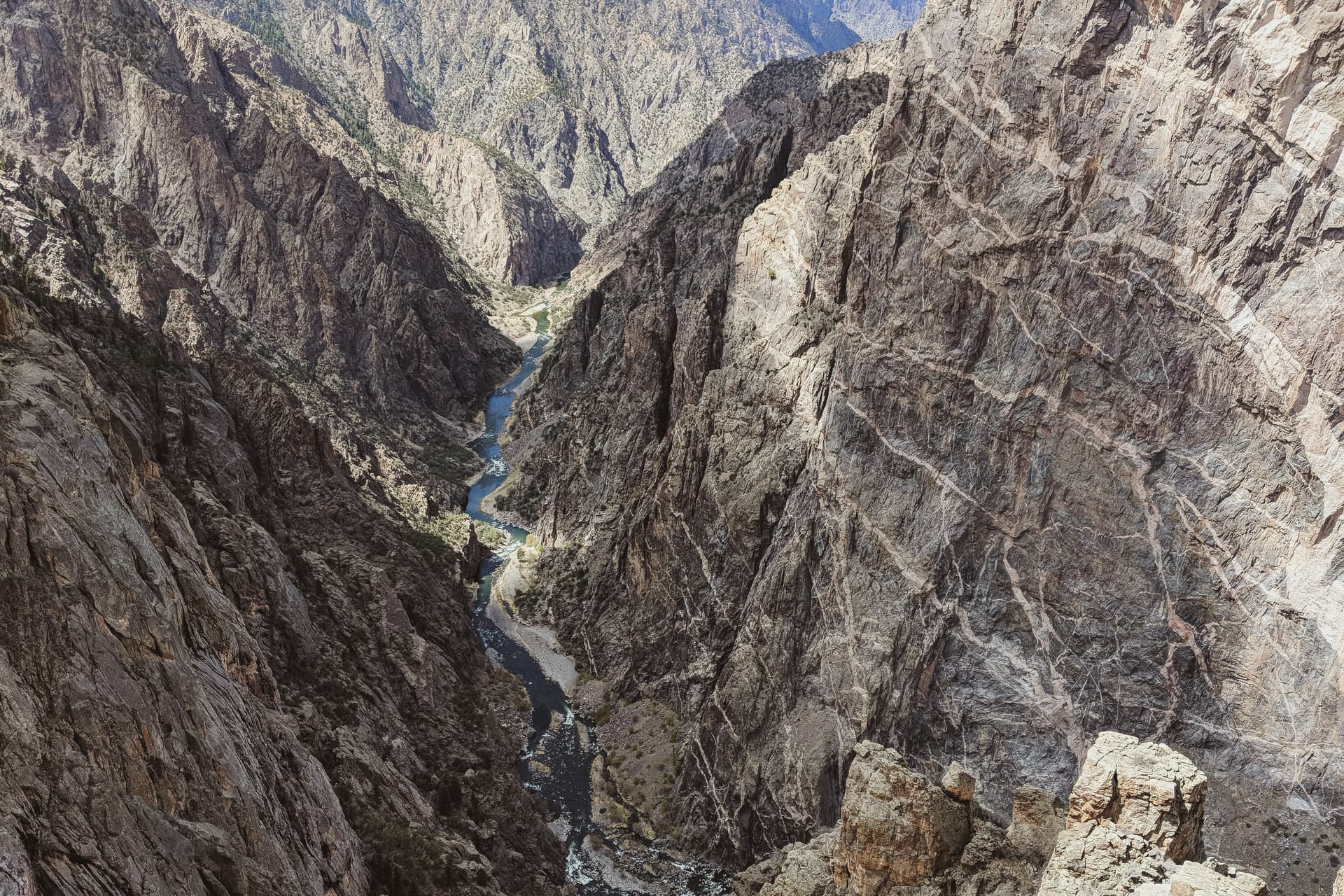 A view down the Gunnison, through the steep, broken walls of the Black Canyon. On the right, one of the dark purple canyon walls is shot through with intrusions of white granite.