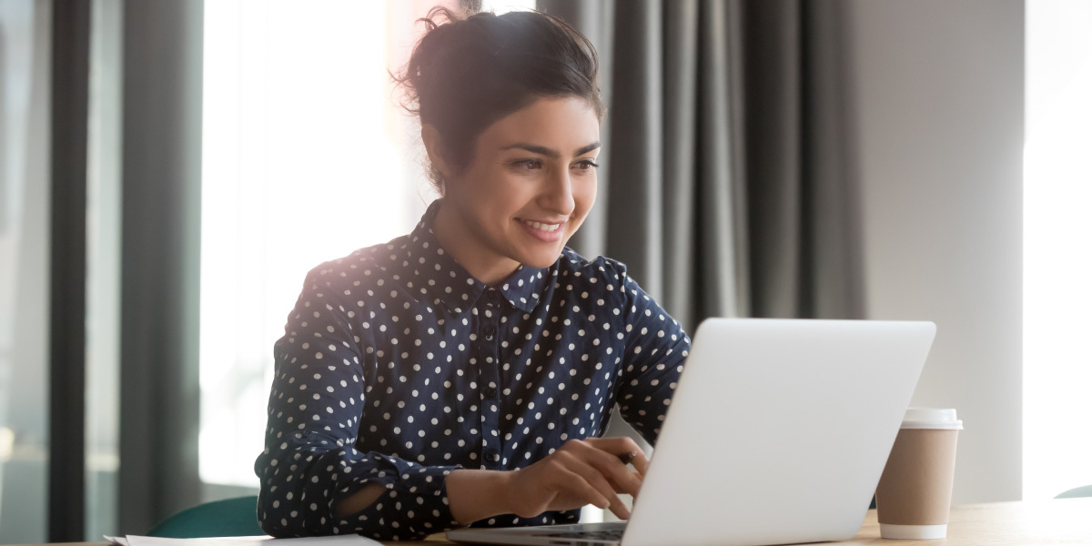 What is the difference between structured and unstructured data? A data analyst smiling looking at a laptop screen with a cup of coffee on the table