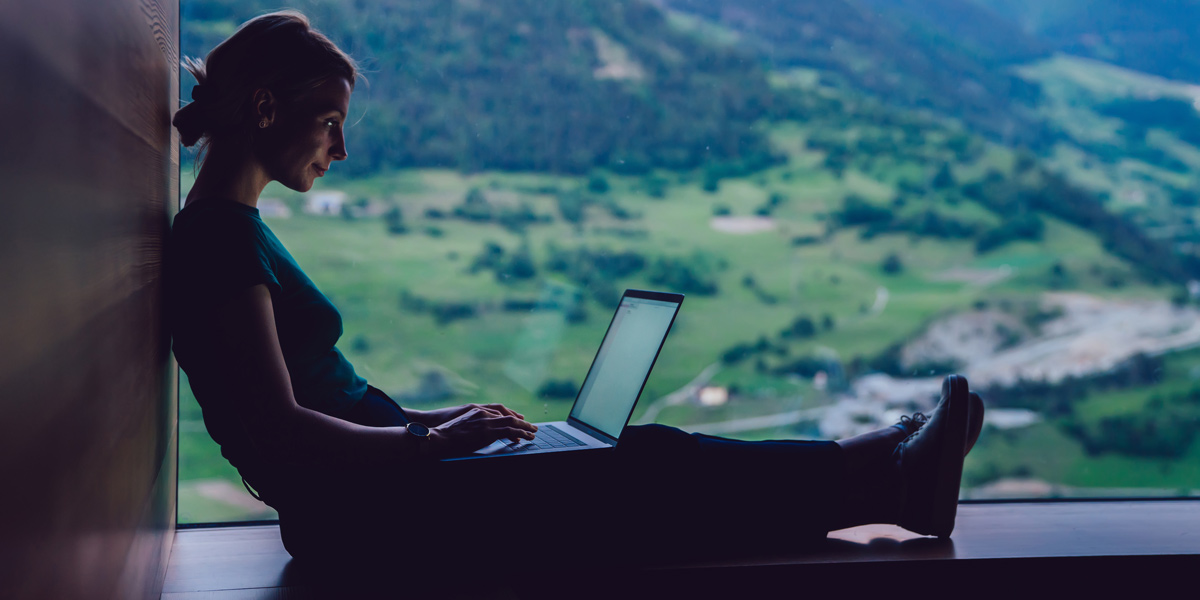 UI designer working on her laptop UI designer sitting on a ledge holding a laptop in the countryside