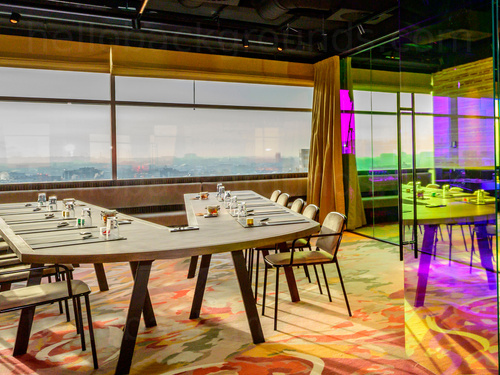 Modern boardroom with large windows and city views containing V shaped table and interior floor to ceiling windows Microsoft Teams background