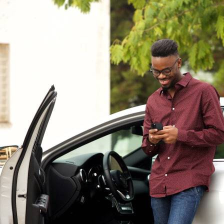 Smartly dressed man leaning against a car looking at his smartphone