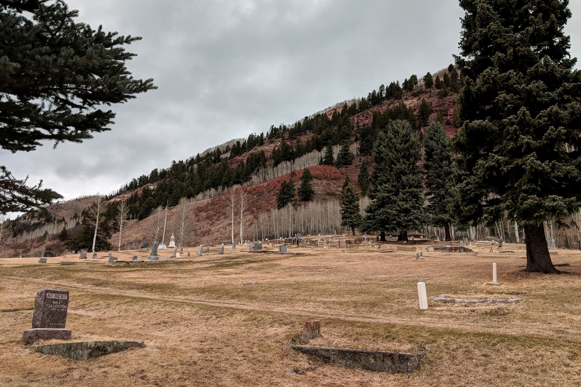 A mountain cemetary. The sky is cold and gray, but some of the bushes on the small rise behind the cemetary are a striking red color.