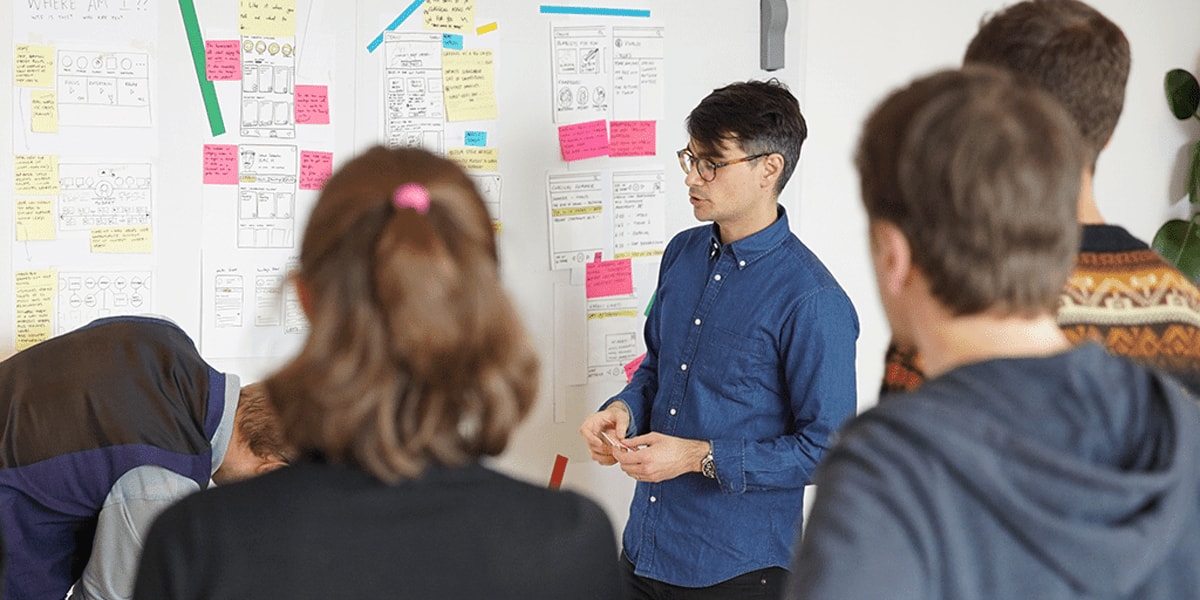 A UX designer reviewing wireframes on a whiteboard A UX design team standing a front of a whiteboard filled with wireframes