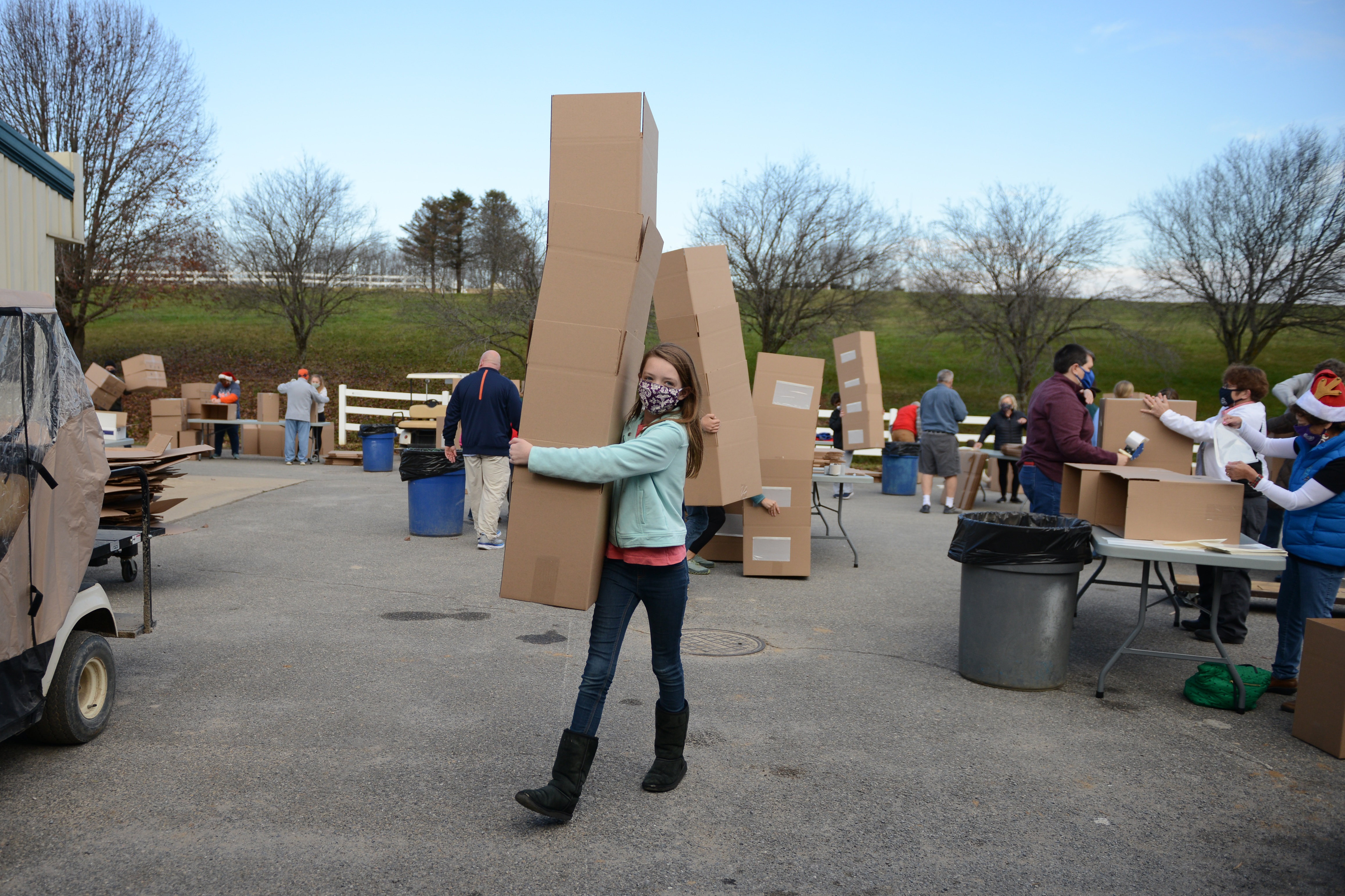 Young female volunteer, masked, with a stack of large cardboard boxes in her arms, headed inside the Virginia Horse Center.