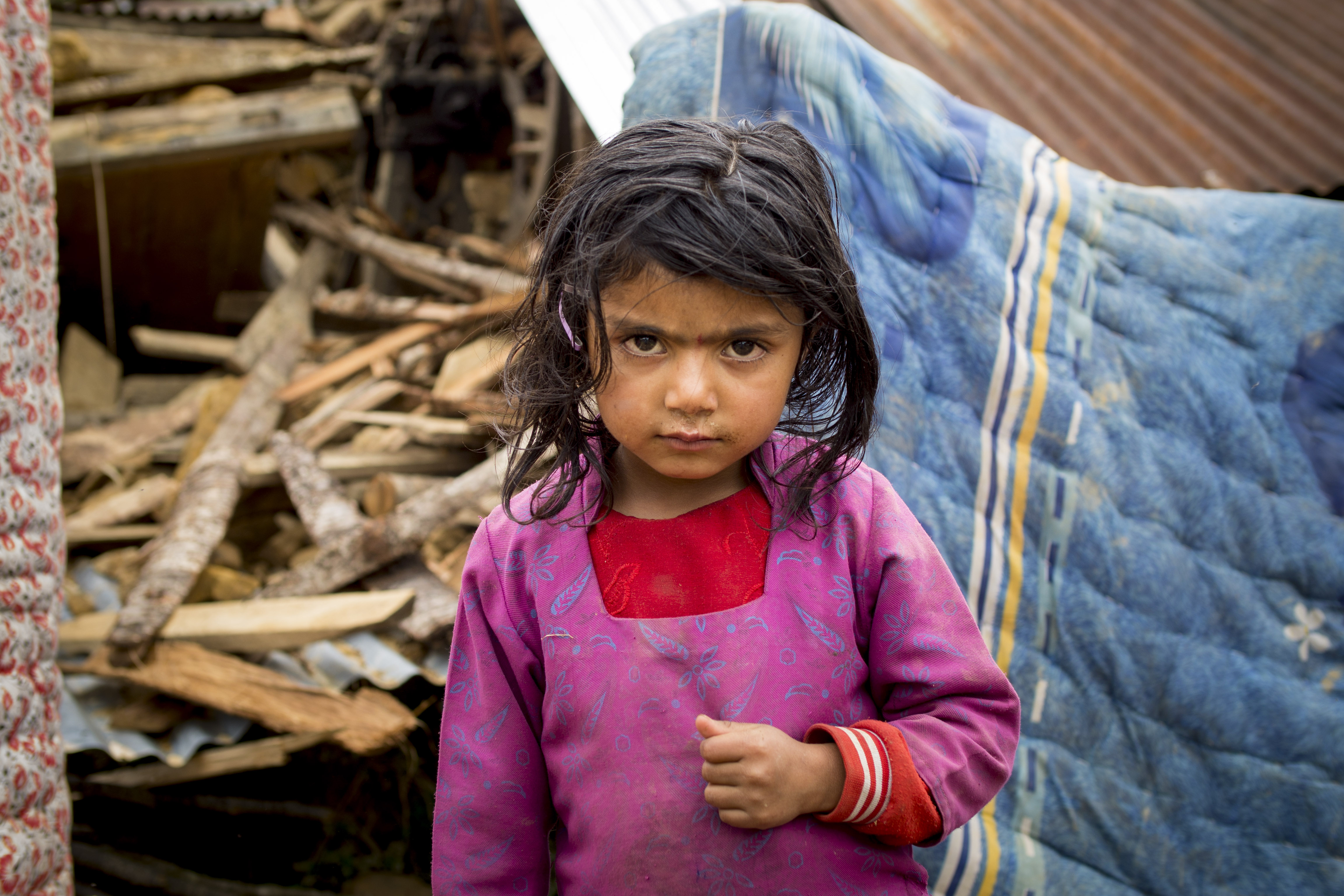 A young girl stands in front of the remains of her home in Kabhrepalanckok district, Nepal, following the 2015 earthquake