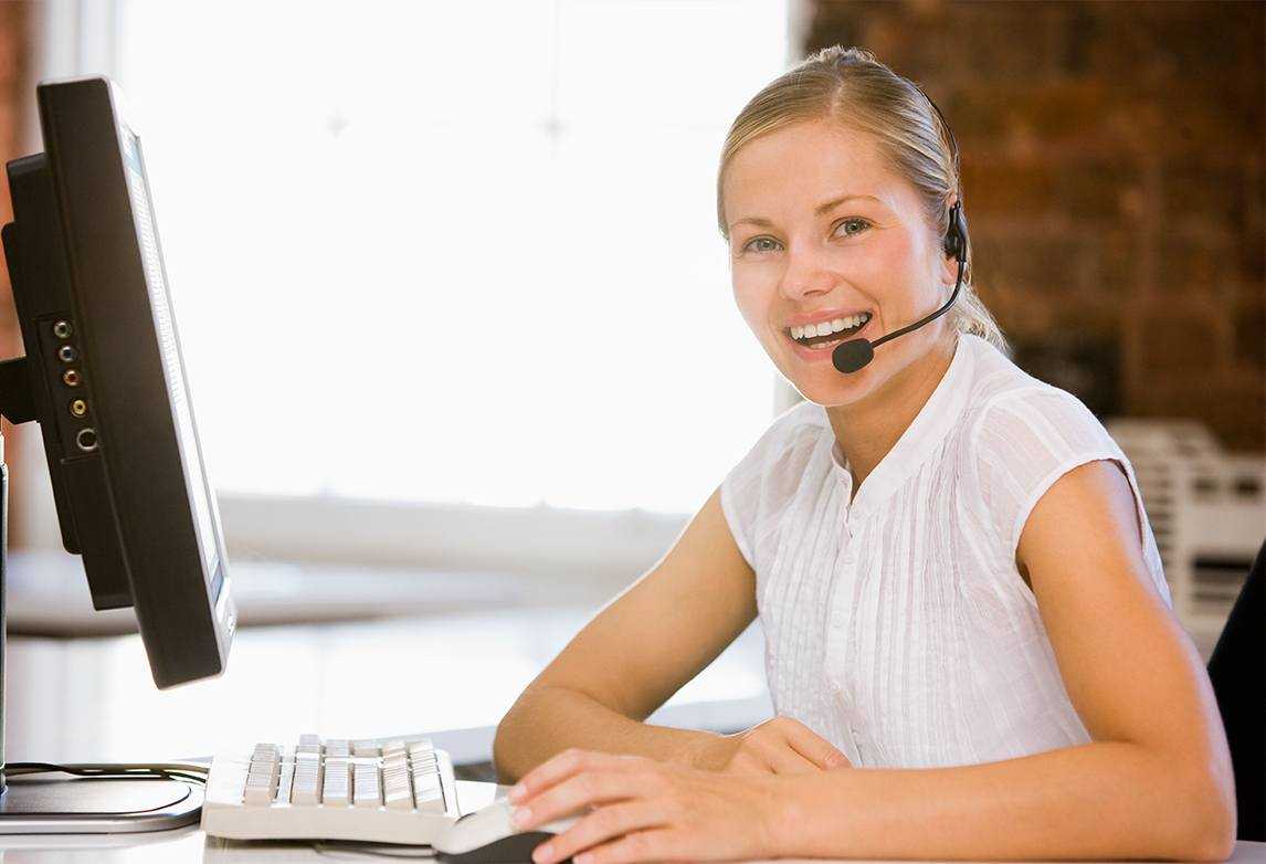A woman wearing a headset smiles while working at a computer.