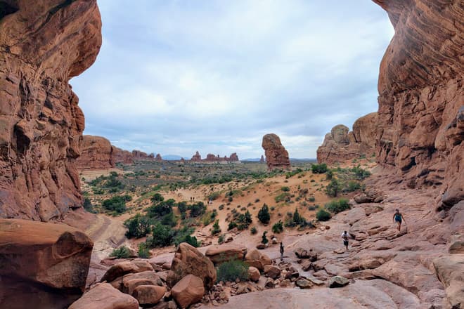 Looking through one of the arches of Double Arch back out towards the rest of Arches National Park. The wide-angle shot makes the arch almost look like a cave. In the foreground, Len watches an approaching group of hikers.