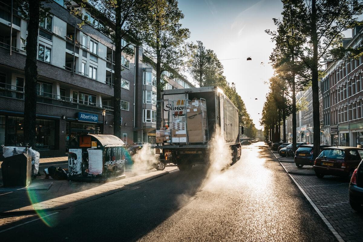 A delivery truck with its cargo door open drives down a street in a European city.