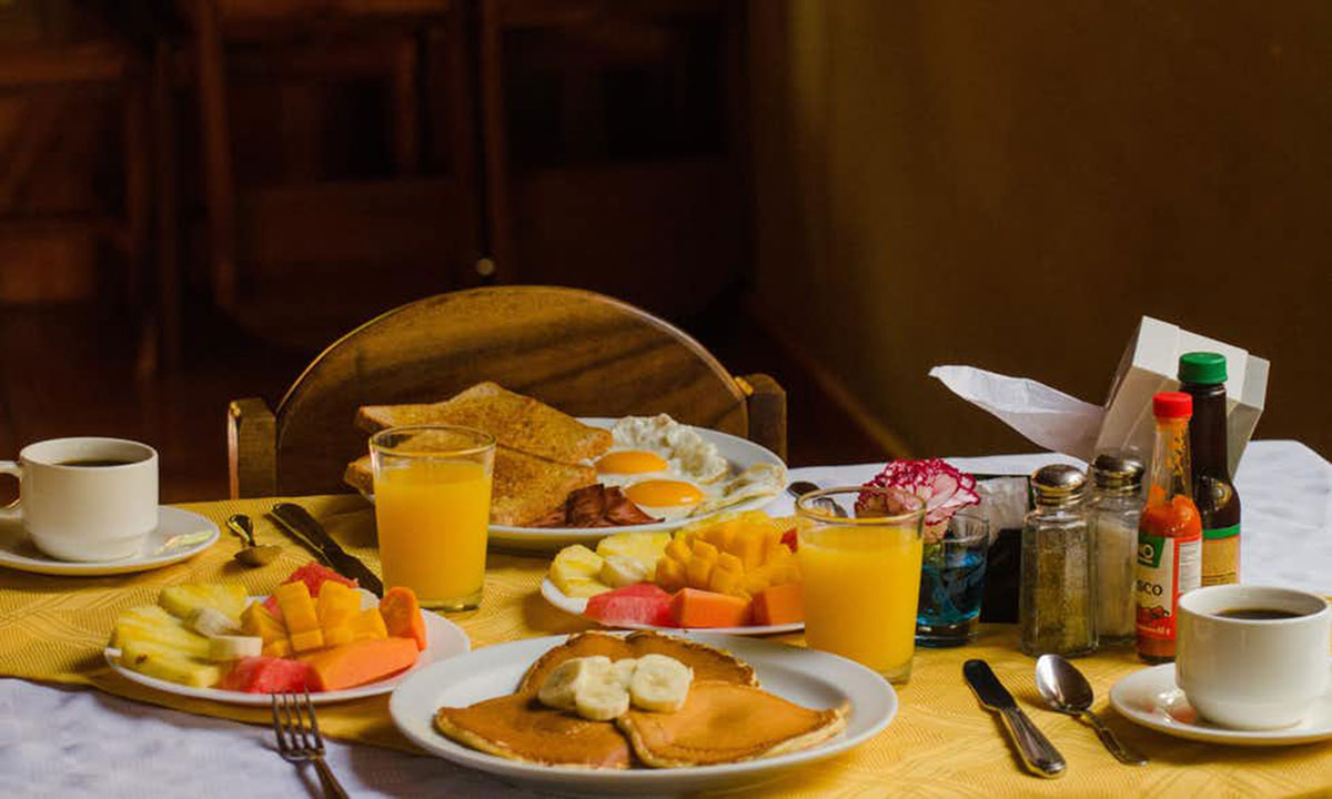 A breakfast of pancakes, fruit, toast, eggs, bacon, juice, and coffee at Los Cipreses Bed and Breakfast