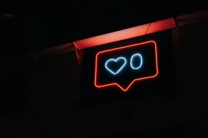 A neon sign in the format of an Instagram like notification. Inside of it there is a heart, followed by the number zero.