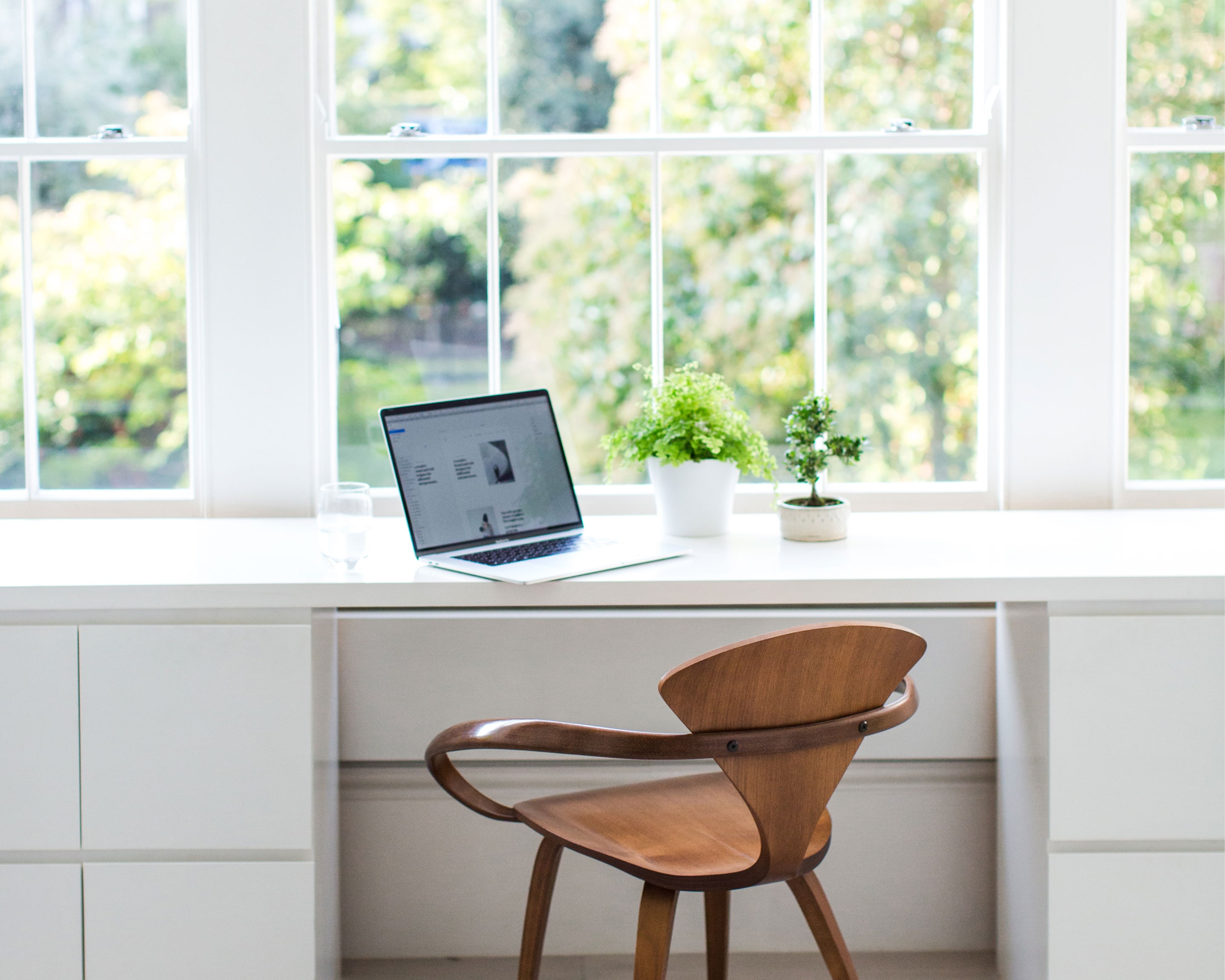 Jack Watkins light filled, bright white office space and desk with minimal styling, plants and MacBook