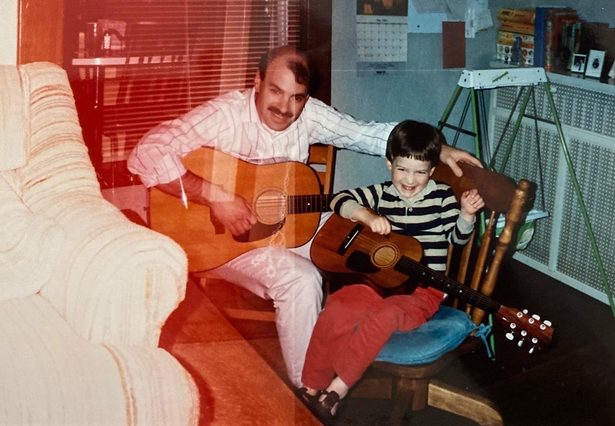 A double exposed photo from the early 90s of a balding man and his young son. The man has a 12 sting acoustic guitar and the boy is playing a miniature 6 string guitar