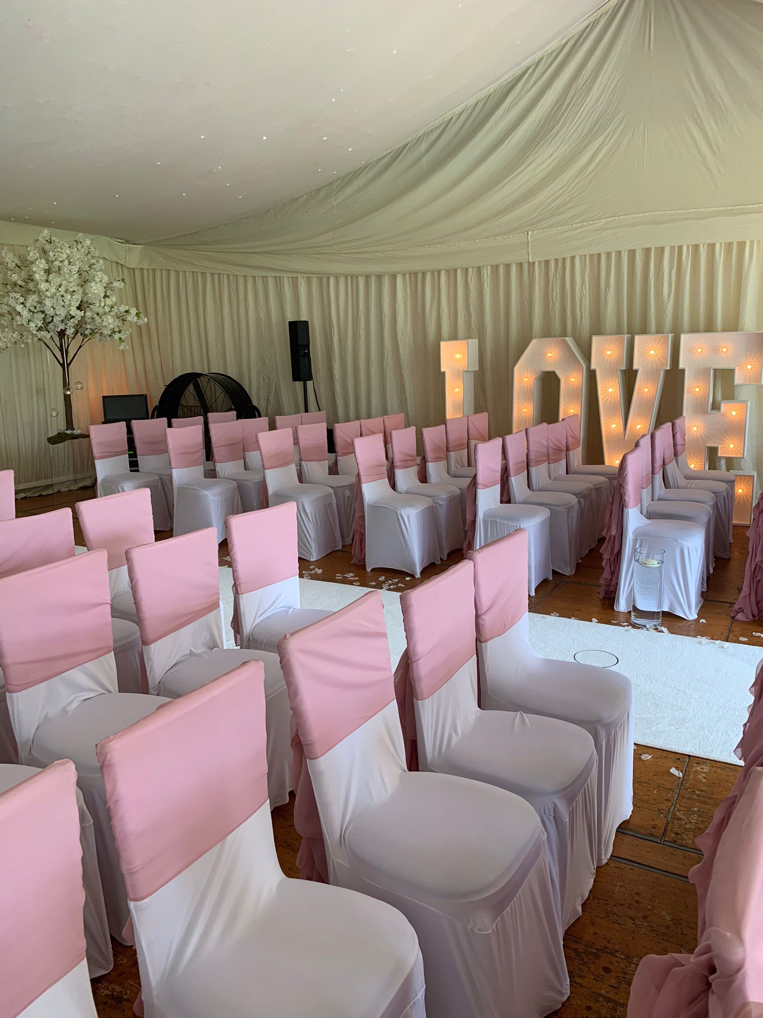 Brilliant pink sashes draped over the back of white chairs. Chairs ready to receive a wedding ceremony