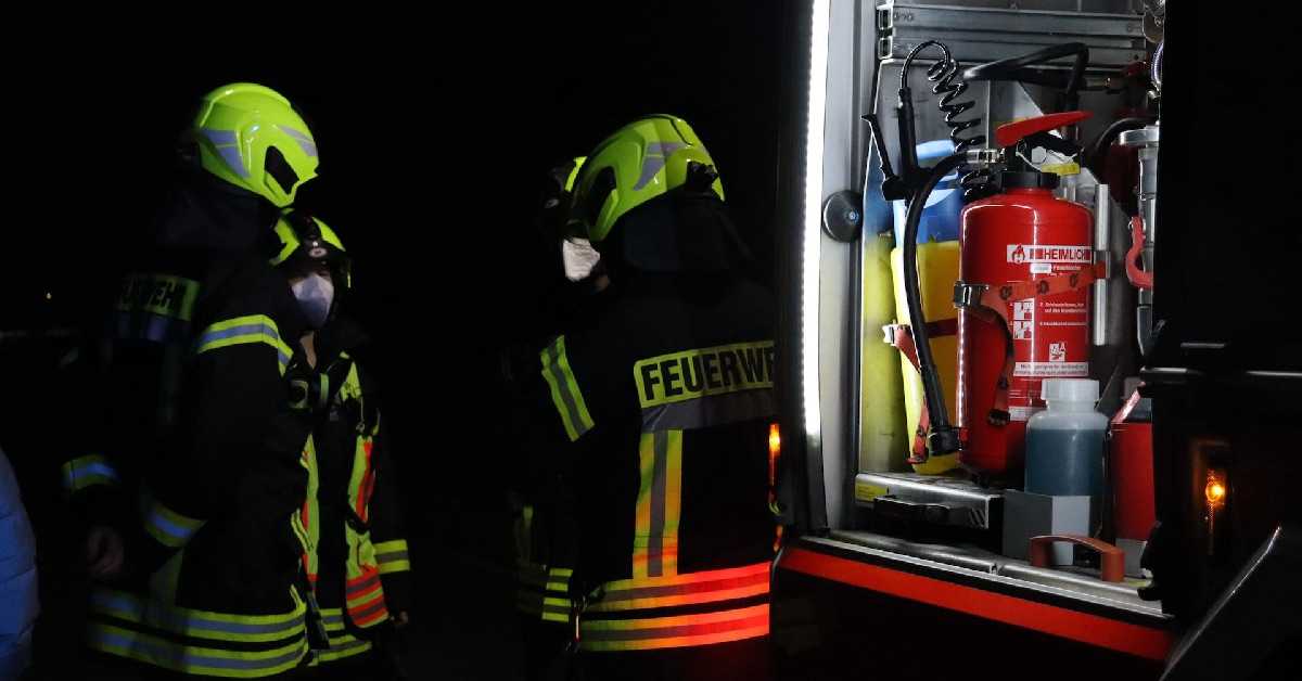 Drei Feuerwehrleute in Uniform unterhalten sich bei einer Feuerwehr Übung vor einem offenen EInsatzfahrzeug