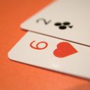 Two overlapping playing cards resting on orange. Tightly cropped to one corner, the cards are six of hearts and two of clubs.