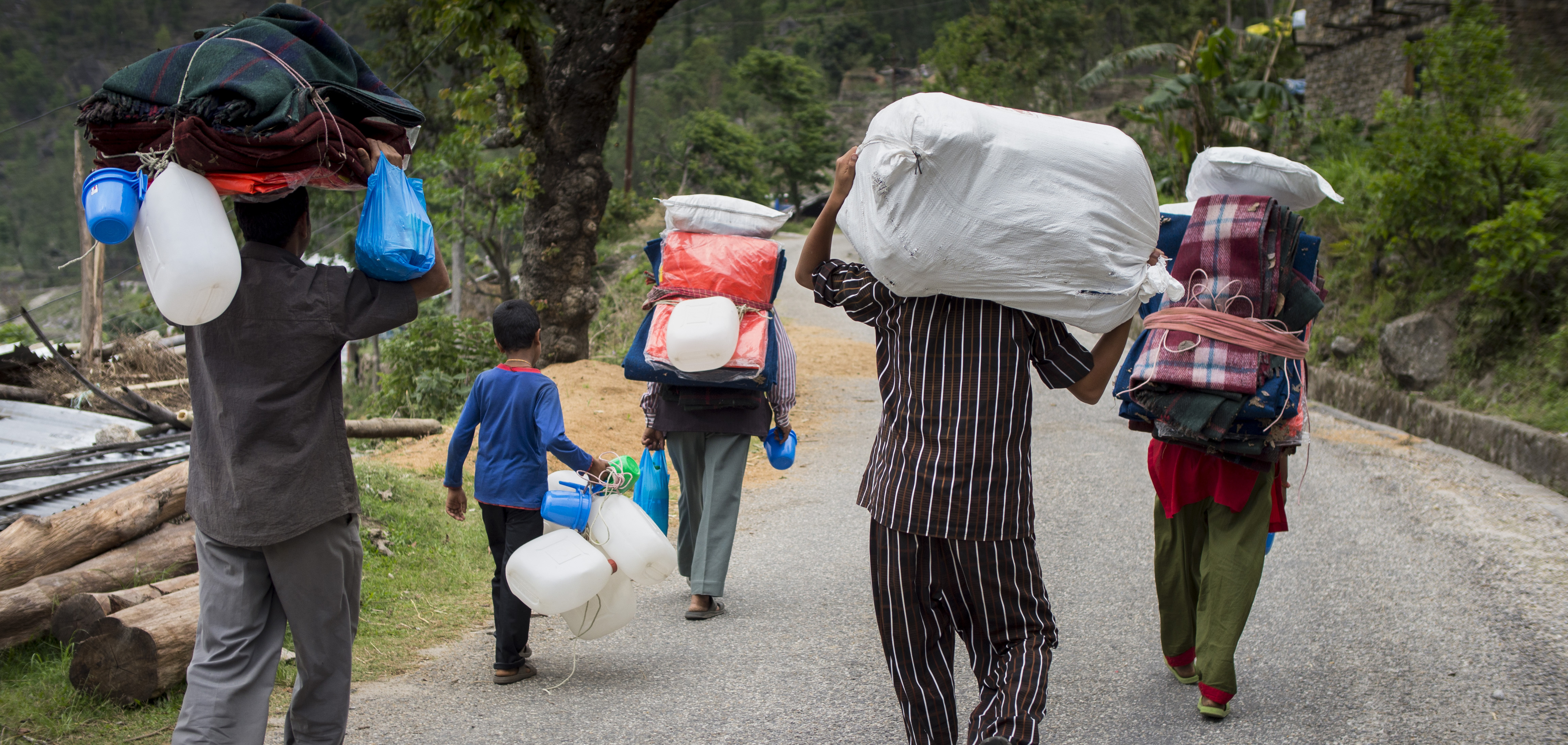 A group of Nepalis displaced by the 2015 earthquake walk away from the camera carrying emergency supplies. 