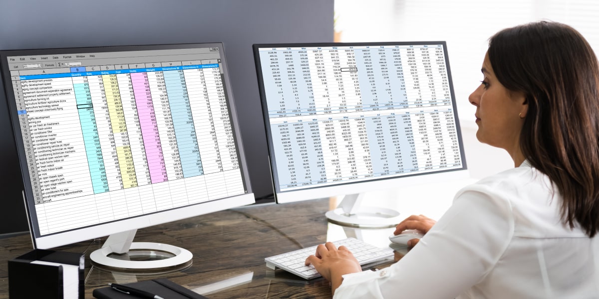 What is the AVERAGE function in Excel and how does it work? A data analyst in side profile, looking at spreadsheets on two computer screens